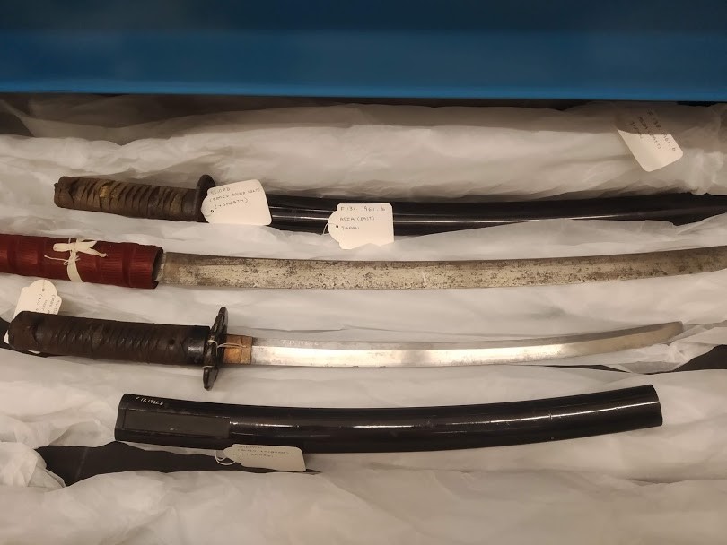 2 swords with their sheaths in a draw in a museum. Each sword and sheath has an object label