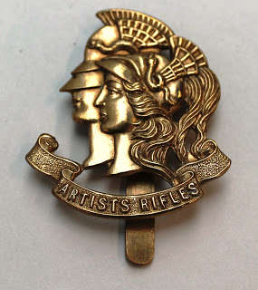 A photograph of a gold badge with 2 people wearing helmets above the phrase Artists Rifles