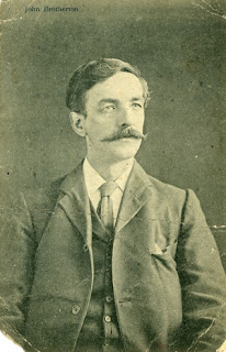 A black and white portrait photograph of a man with moustaches