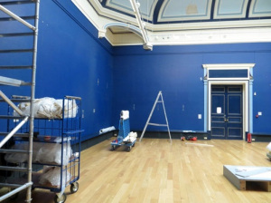 A blue gallery space filled with ladder and scaffolding