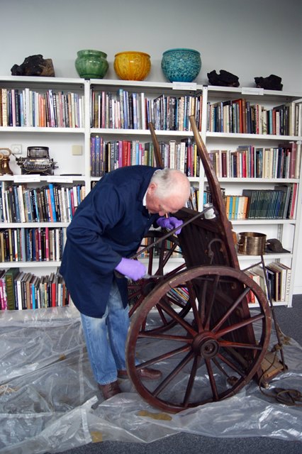A man cleaning a large wooden cart.