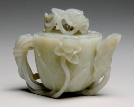 a small pot that looks like a tea pot made of pale jade, wih an elaborate lotus leaf design.