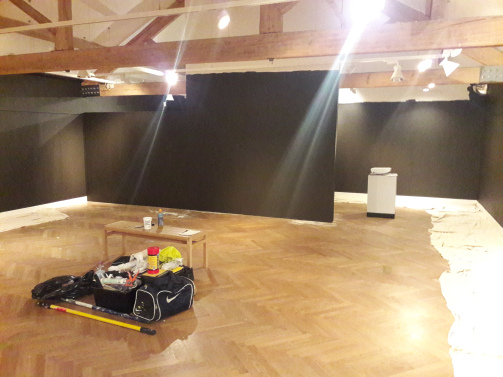 a large open space with nothing in it except painting tools - the walls of the space are painted very dark grey.