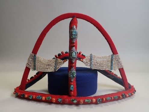 a red headdress mounted on a dark blue stand. The headdress is covered in turquoise stones and looks very intricate.