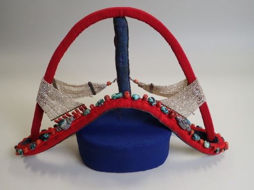 A red headdress mounted on a dark blue stand. The headdress is covered in turquoise stones and looks very intricate.