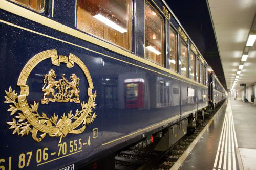 An ornate blue train with a gold crest waits on the platform of a train station,