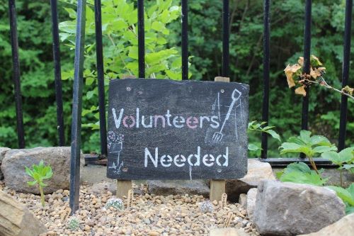 A blackboard sign in the garden says 'volunteers needed'.