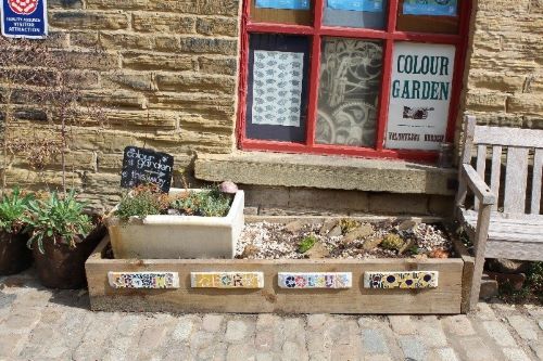 A plant box outside the front of the stone building of the Mill has a colourful sign saying 'plant for colour'. It is a sunny day. 