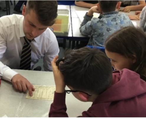 A teacher is pointing at an object on a table and sitting with two pupils.