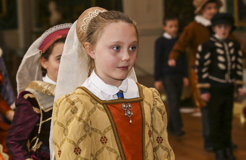 A young girl and other children are dressed up in Tudor costume and stood in a line in a hall within Temple Newsam House