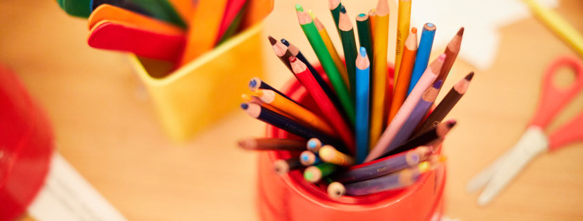 coloured pencils are sitting in a red pot on a wooden table surrounded by other craft materials