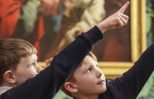 Two young boys in school uniform point at paintings in an elaborately decorated room