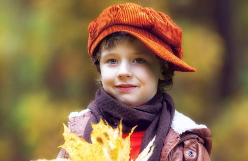 A child in woodland holding a bunch of yellow leaves