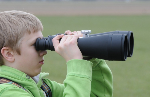 A boy wearing a green hoodie looking through oversized binoculars