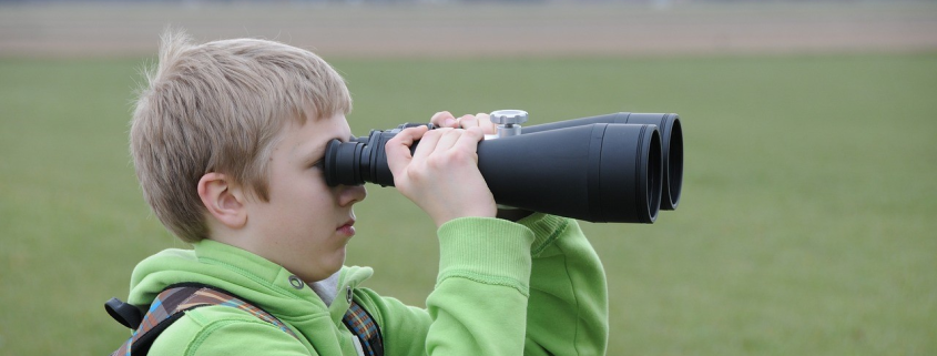 A boy wearing a green hoodie looking through oversized binoculars