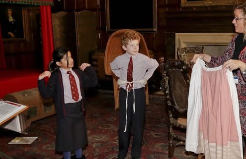 Two children in school uniform are dressing up in period costumes.