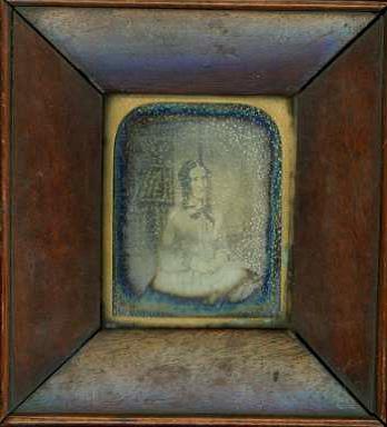 A dark wooden frame with a very faint, blue tinted image of a Victorian woman in the centre. You can see that her hair is in ringlets.
