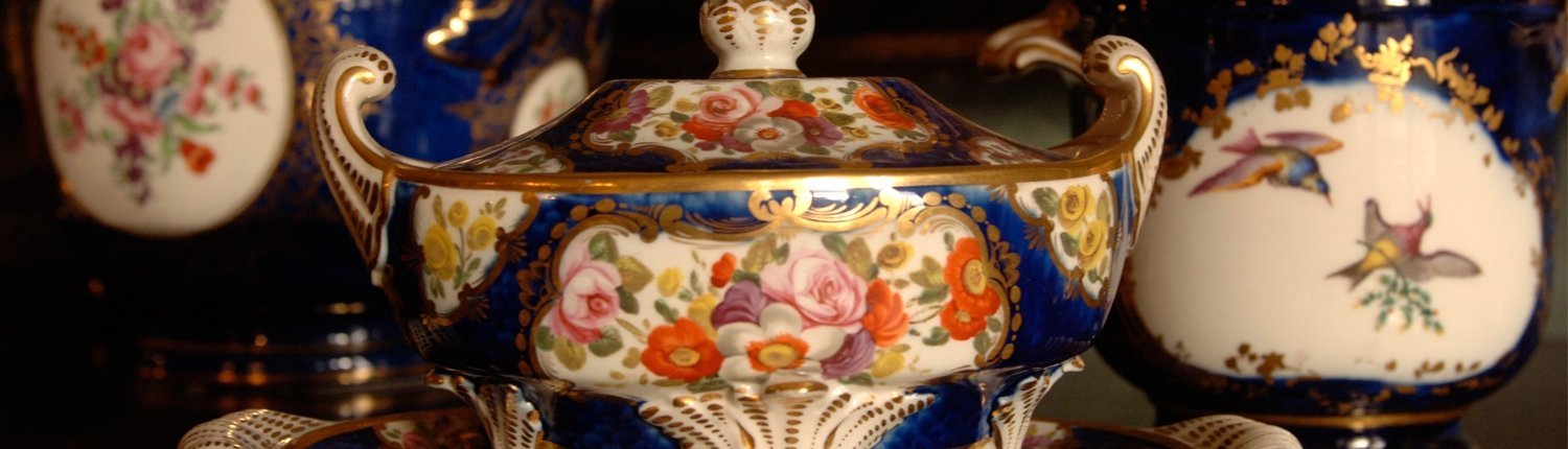 A ceramic dish. It is painted blue, has a gold handle and trimmings and has flowers painted in the middle.
