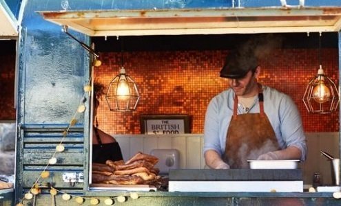 Man in street food vendor truck next to a pile of giant Yorkshire puddings