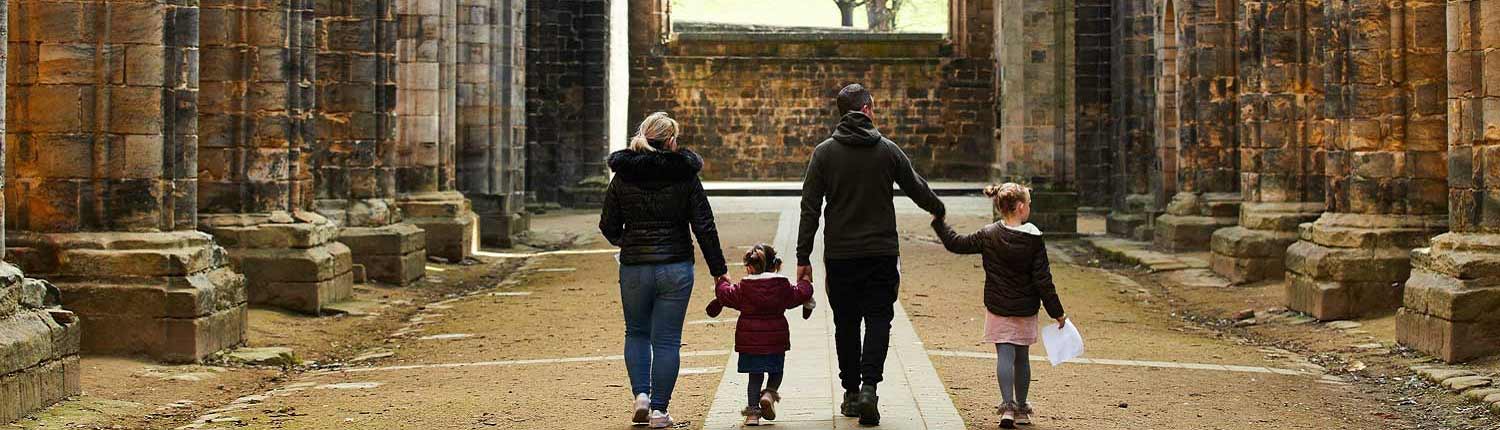 Family of four holding hands walking inside Kirkstall Abbey