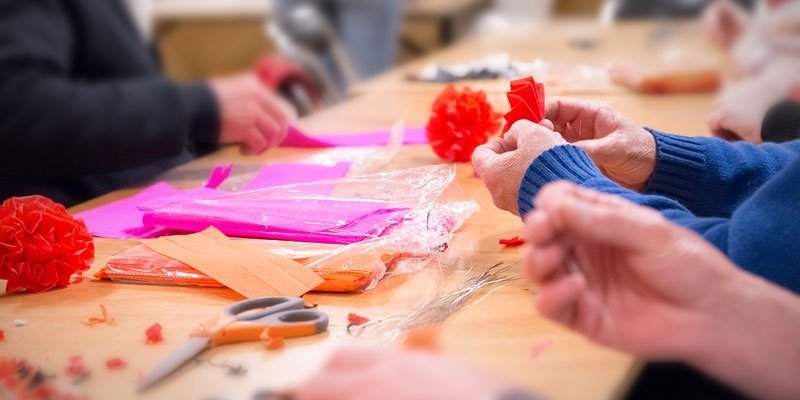 A close up of adults hands making decorations from craft paper at a table