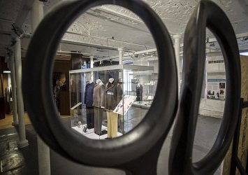 Outfits in display cases, pictured through the handle of a pair of scissors