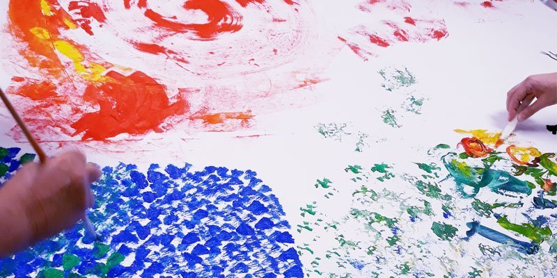 Two people are painting colourful swirls on a large white piece of paper.