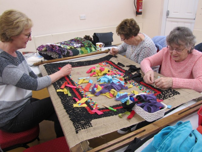 Image of volunteers working on the traditional rag rug on display