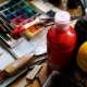 A selection of arts and crafts materials laid out on a table including colouring pencils, paint and paint brushes