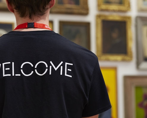 A staff member stood with his back to the camera wearing a t-shirt which says WELCOME across the back of it.