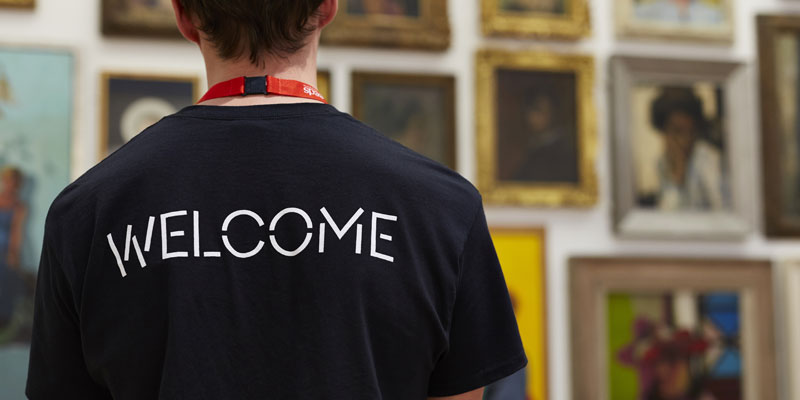 A staff member stood with his back to the camera wearing a t-shirt which says WELCOME across the back of it.