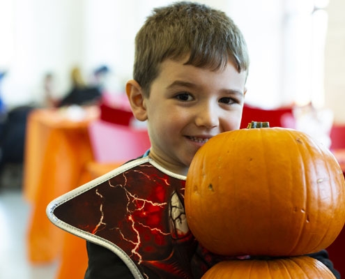 A young boy dressed up in costume for Halloween carrying two pumpkins