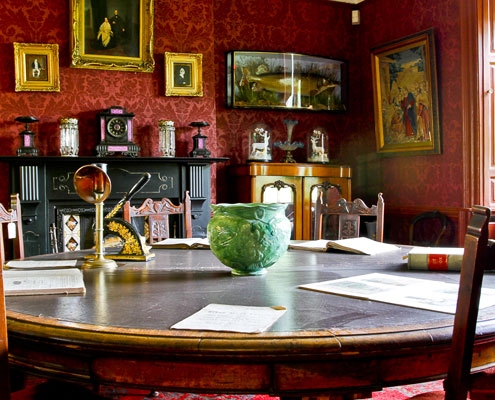 The interior of the old office / dining area of the Mill Managers cottage in Leeds Industrial Museum including vintage furniture, original fireplace, red wallpaper and various works of fine art