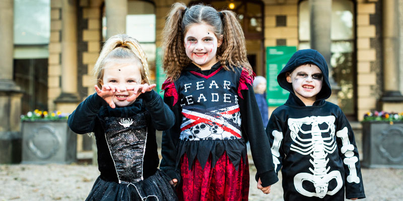 Three children dressed up for Halloween as witches and skeletons