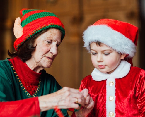 A lady dressed as an elf taking part in Christmas crafts with a little boy wearing a santa suit