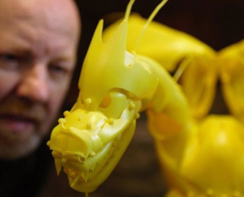 Artist looking at a yellow dragon model crafted from recycled plastic materials