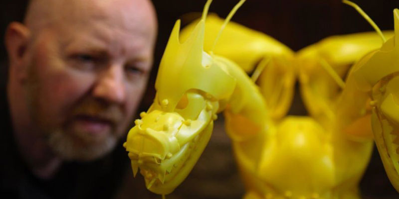 Artist looking at a yellow dragon model crafted from recycled plastic materials