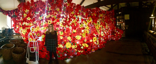 A woman is standing in front of a wall of handmade yellow and red poppies.