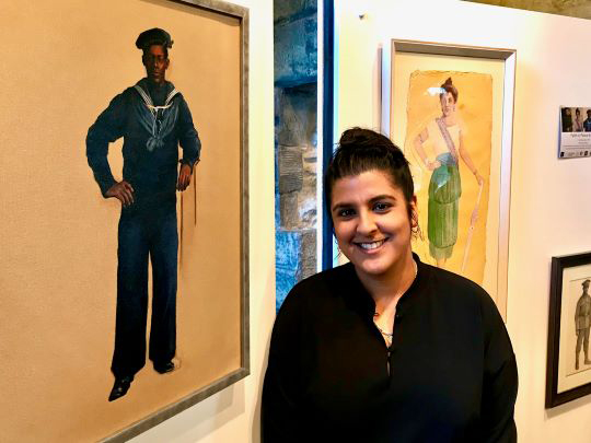 An artist is standing in front of two full length portrait paintings.
