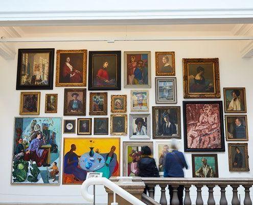 Visitors admiring a wall of brightly colored portrait paintings in an art gallery