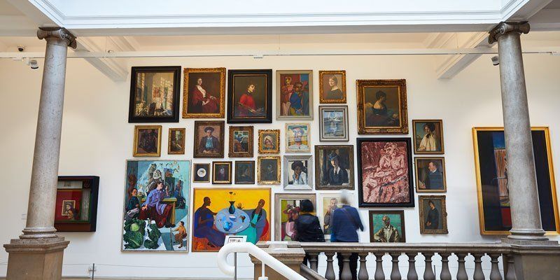 Visitors admiring a wall of brightly colored portrait paintings in an art gallery
