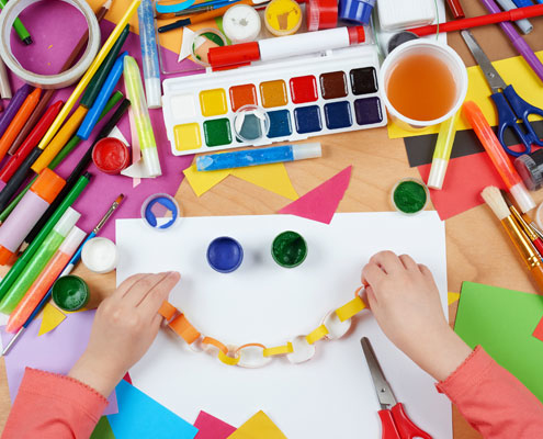 A child using different materials to create a smiley face on a piece of paper, also surrounded by crafting materials in different colours.
