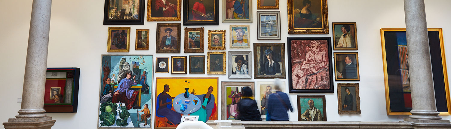 Visitors looking at a wall of bright portrait paintings displayed above a staircase