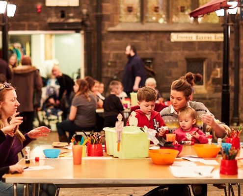 A group of people including adults and children taking part in craft activities in the Victorian Streets at Abbey House Museum
