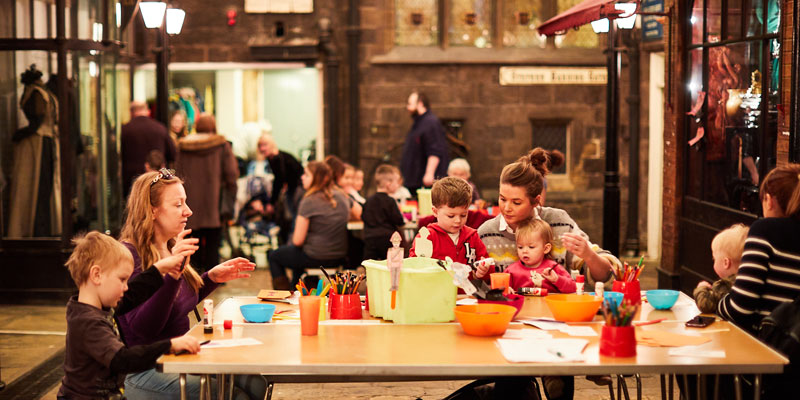 A group of people including adults and children taking part in craft activities in the Victorian Streets at Abbey House Museum
