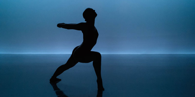 A contemporary dance performance with the silhouette of a dancer against a blue background