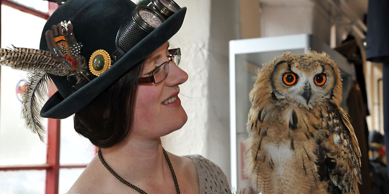 A woman dressed as a steampunk holding and looking at a large brown owl