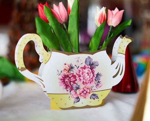 A handmade paper teapot with flower decoration which has been filled with pink tulips