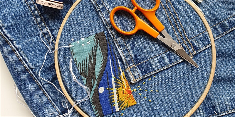 A denim garment with hand embroidery across one section, an embroidery ring and scissors.