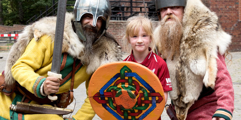 Two bearded men dressed as an Anglo saxons on either side of a child holding a cardboard shield